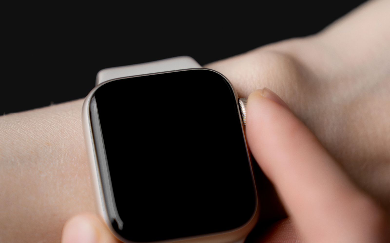 Een pols met een smartwatch, scherm uit, tegen een donkere achtergrond